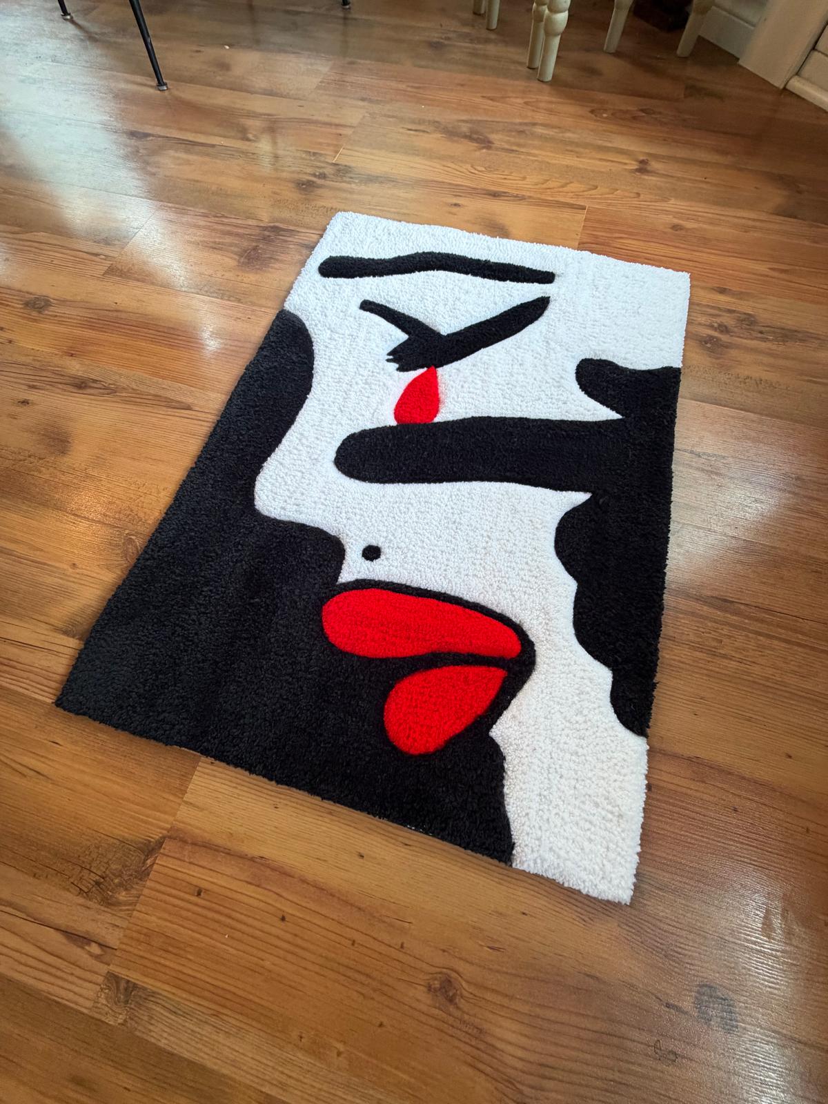Hand-tufted abstract face rug in black and white with red lips and tear, angled view